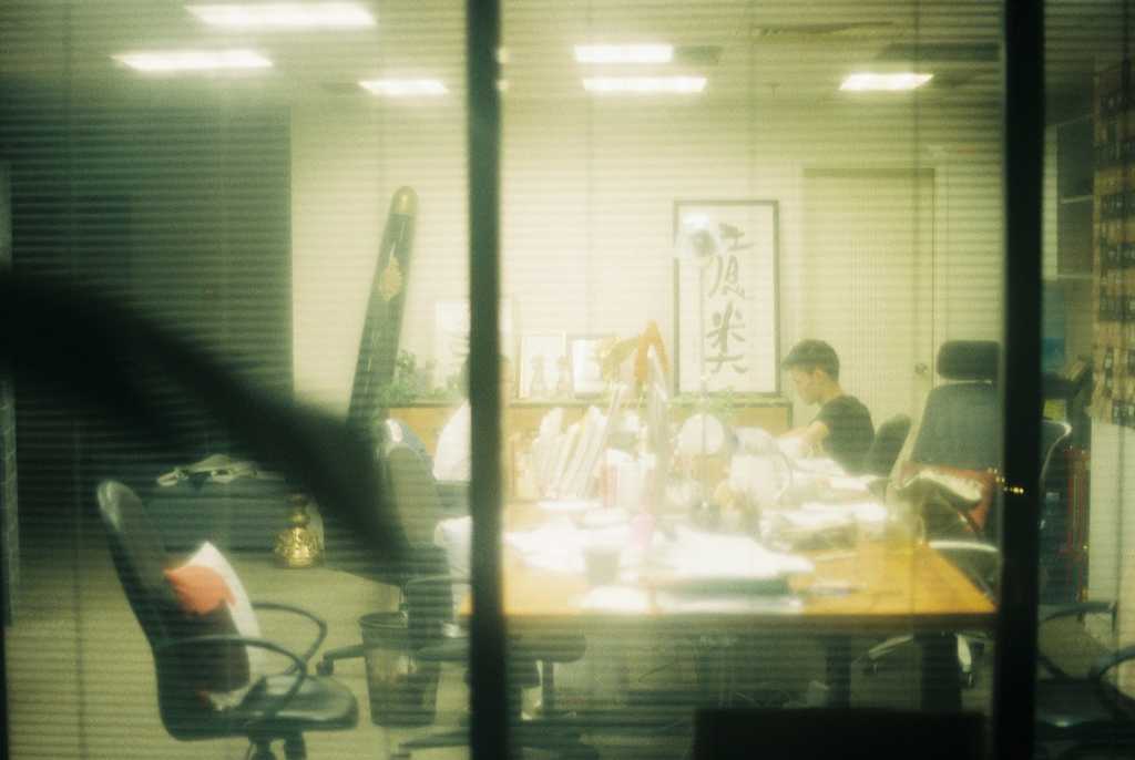 Blurred view through office glass walls of a busy team working late in a cluttered workspace, symbolizing the overwhelming volume of medical marketing data and the opportunity to transform it through AI-powered solutions.