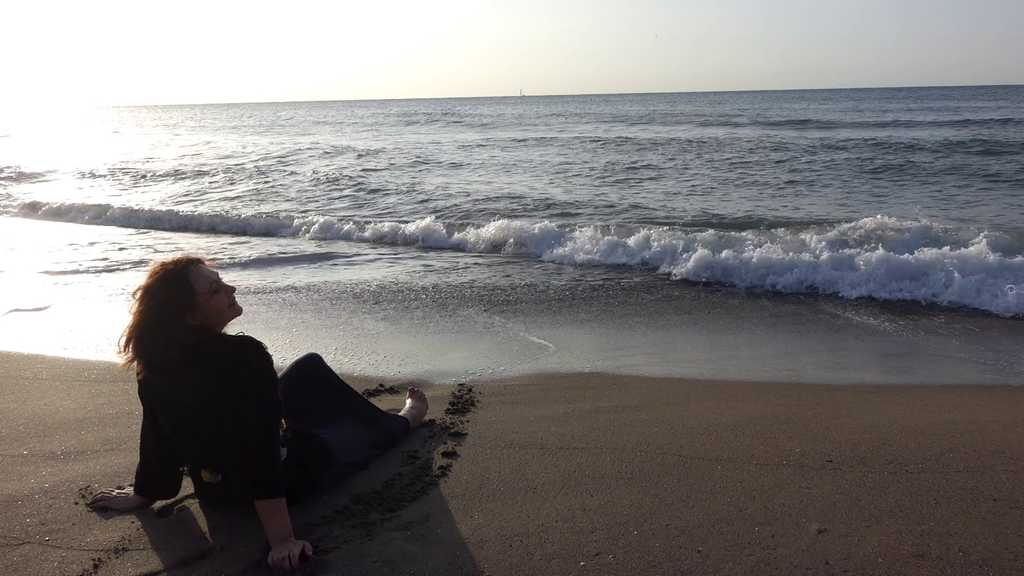 Actress resting barefoot on the shore after a cathartic moment during the ZAO Studio Carnival improvisation, symbolizing emotional release, transformation, and the completion of the Dulcinea character arc.