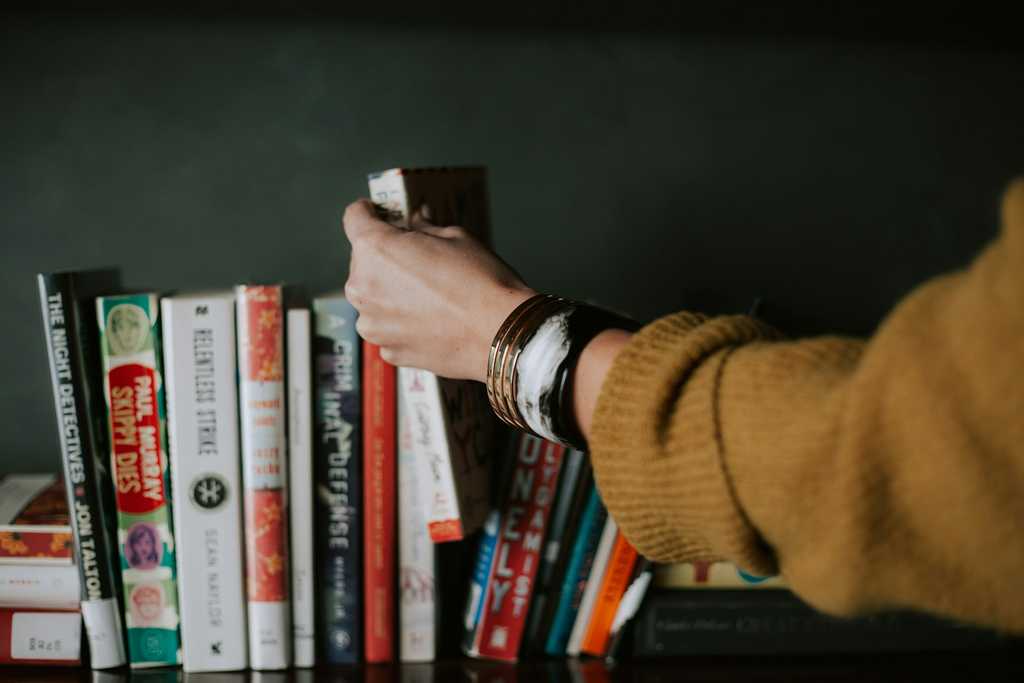 A person’s hand selecting a book from a shelf filled with colorful books, symbolizing the careful curation and thoughtful approach involved in shaping innovative AI solutions for medical data management.