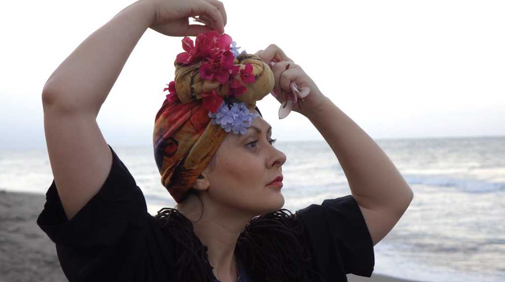 Close-up of actress preparing the Dulcinea character headpiece with vibrant flowers by the sea, showcasing the costume creation and embodiment process for the ZAO Studio Summer Carnival improvisation project.